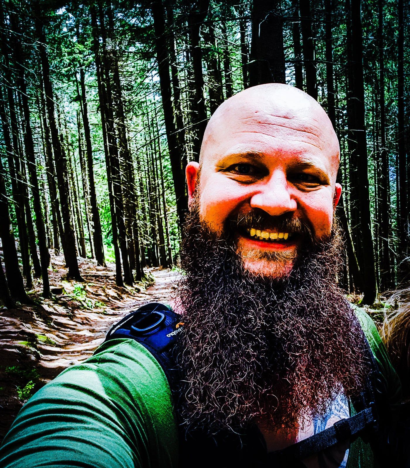 Porträt von Thorsten mit langem Vollbart, lachend beim Wandern im Wald
